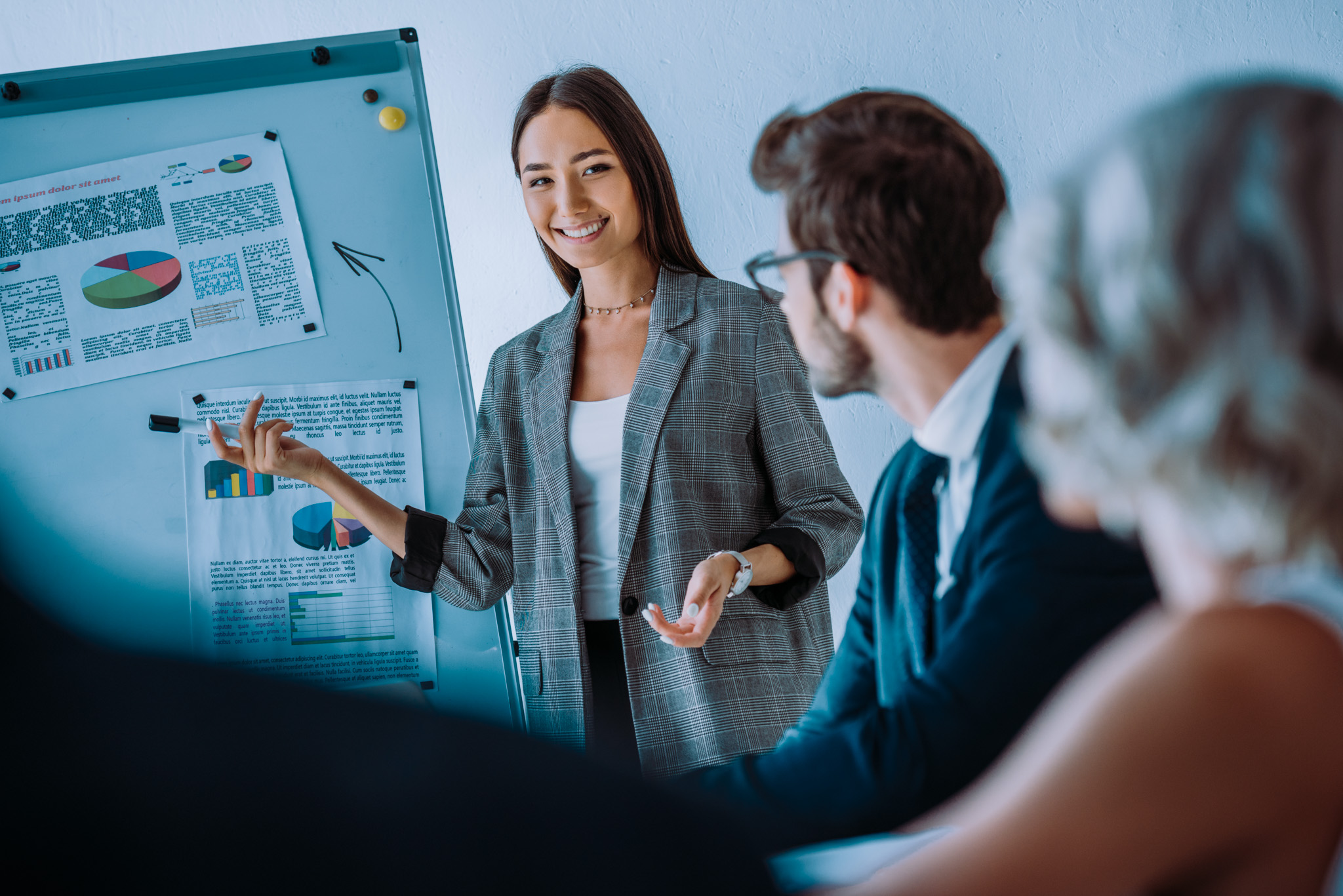 smiling asian businesswoman pointing on flipchart during meeting in office