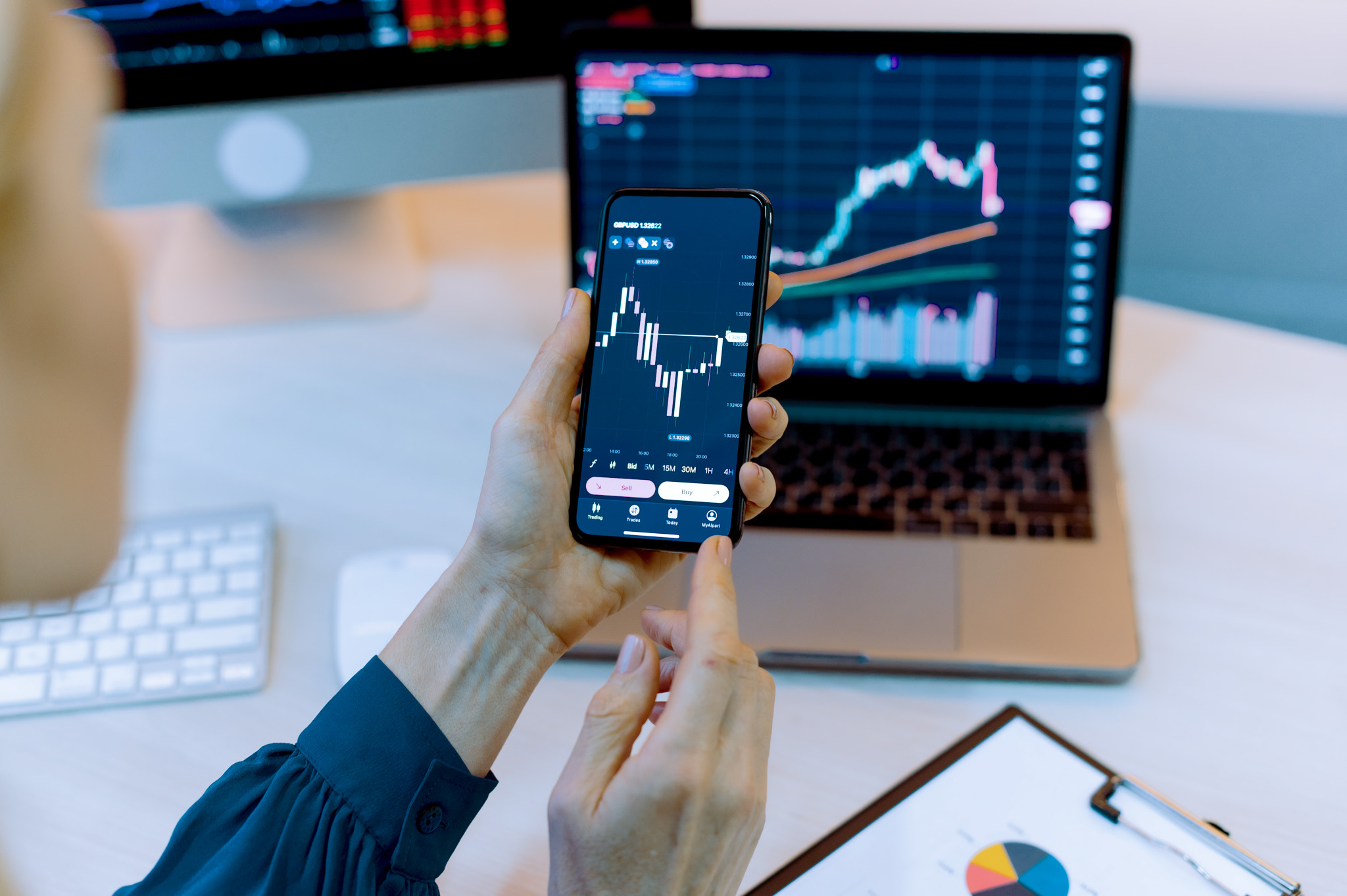 Close-up laptop and cellphone screen with stock diagrams. Female crypto trader investor broker using cellphone and laptop for cryptocurrency financial market analysis, buying or selling